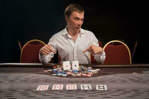 bonito emocional homem é jogando pôquer sentado às a mesa dentro casino. foto