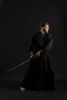 kendo guru vestindo dentro uma tradicional japonês quimono é praticando marcial arte com a Shinai bambu espada contra uma Preto estúdio fundo. foto