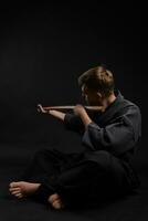 kendo guru vestindo dentro uma tradicional japonês quimono é praticando marcial arte com a Shinai bambu espada contra uma Preto estúdio fundo. foto