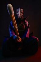 fechar acima. kendo lutador vestindo dentro a armaduras, tradicional quimono, capacete, sentado, praticando marcial arte com Shinai bambu espada, Preto fundo. foto