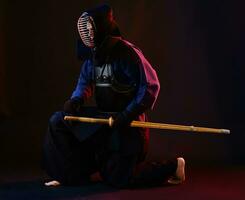 fechar acima tomada, kendo lutador vestindo dentro a armaduras, tradicional quimono, capacete praticando marcial arte com Shinai bambu espada, Preto fundo. foto