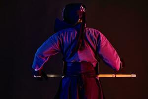 fechar acima. kendo lutador vestindo dentro a armaduras, tradicional quimono, capacete praticando marcial arte, Shinai bambu espada, em pé voltar, Preto fundo. foto