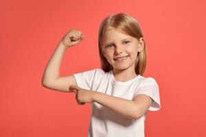 fechar-se estúdio tiro do uma agradável Loiras pequeno menina dentro uma branco camiseta posando contra uma Rosa fundo. foto