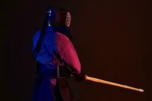 fechar acima tomada, kendo lutador vestindo dentro a armaduras, tradicional quimono, capacete praticando marcial arte com Shinai bambu espada, Preto fundo. foto