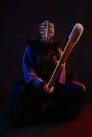 fechar acima. kendo lutador vestindo dentro a armaduras, tradicional quimono, capacete, sentado, praticando marcial arte com Shinai bambu espada, Preto fundo. foto