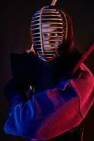 fechar acima tomada, kendo lutador vestindo dentro a armaduras, tradicional quimono, capacete praticando marcial arte com Shinai bambu espada, Preto fundo. foto