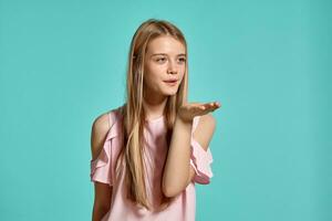 estúdio retrato do uma lindo menina Loiras adolescente dentro uma Rosa camiseta posando sobre uma azul fundo. foto