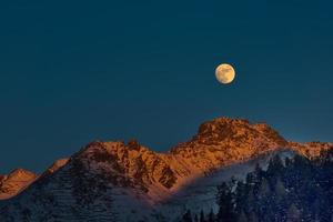 lua cheia ao pôr do sol nas montanhas de inverno foto