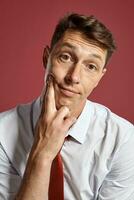 retrato do uma jovem moreno homem posando dentro uma estúdio contra uma vermelho fundo. foto