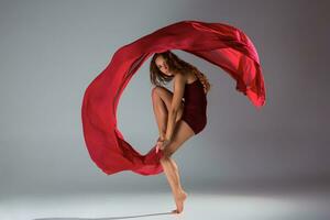 jovem lindo mulher dançarino dentro vermelho roupa de banho posando em uma luz cinzento estúdio fundo foto