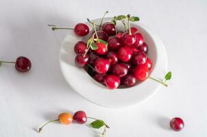 branco copo com maduro vermelho cerejas em uma mesa, verão colheita do frutas e bagas foto