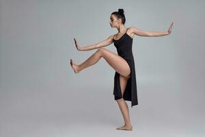 dançando bailarina dentro uma Preto vestir. contemporâneo gracioso desempenho em uma cinzento fundo. foto