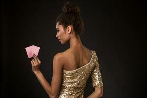 mulher ganhando - jovem mulher dentro uma elegante ouro vestir segurando dois cartões, uma pôquer do ases cartão combinação. foto