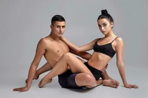 a casal do uma jovem moderno balé dançarinos dentro Preto ternos estão posando sobre uma cinzento estúdio fundo. foto