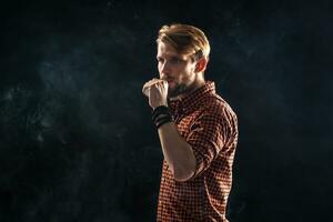 uma jovem homem com uma barba e uma à moda Penteado dentro uma camisa, fumar uma cigarro, uma víbora, uma sala, uma estúdio, fumaça, prazer foto