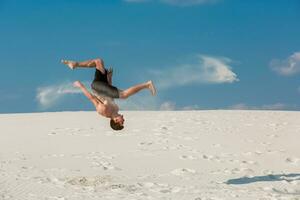 retrato do jovem Parkour homem fazendo giro ou cambalhota em a areia. foto