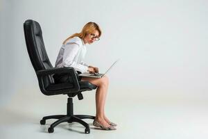 jovem mulher sentado em a cadeira e usando computador portátil foto