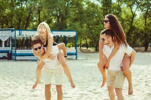 grupo do amigos caminhando ao longo a praia, com homens dando pegar carona passeio para amigas. foto