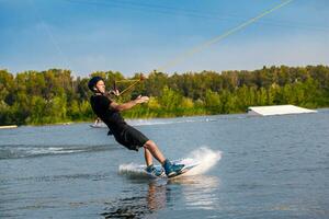 focado homem deslizante em prancha de wakeboard em água superfície segurando rebocar corda com 1 mão foto