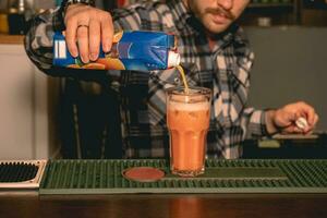 barman derramando laranja suco para alta vidro com gelo foto