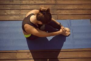 topo Visão do uma mulher dentro Preto topo e perneiras praticando ioga realizando ioga-asanas em uma esteira deitado em uma de madeira chão. foto