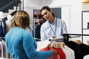 africano americano cliente Perguntando trabalhador para ajuda, discutindo camisa material dentro roupas loja. viciado em compras mulher querendo Novo guarda-roupa, compras para elegante mercadoria dentro moderno boutique foto