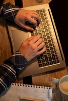 jovem homem bebendo café dentro cafeteria e usando computador portátil. do homem mãos usando computador portátil durante café pausa foto