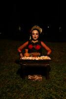 Largo tiro do a ásia menina dentro tradicional roupas sentado dentro uma floresta com uma mesa cheio do flores foto