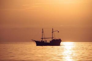 a silhueta de um velho navio com mastros contra o pôr do sol foto