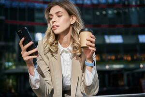 à moda corporativo mulher dentro terno, bebidas dela café Leve embora e usa Móvel telefone aplicativo foto