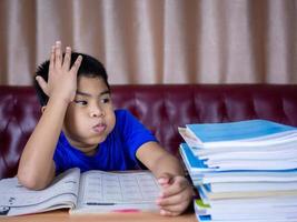 um menino está cansado de ler um livro sobre uma mesa de madeira foto