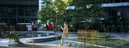 silhueta do corporativo mulher dentro terno caminhando ao longo cidade Centro perto escritório edifícios foto