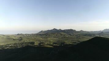 aéreo Visão do a pequeno assentamento dentro verde colinas com Alto montanha cadeia e azul mar em a fundo contra azul céu. tomada. lindo colorida panorama. foto