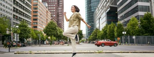 retrato do ásia feliz menina pulando e dançando dentro cidade Centro, posando em ruas, expressar alegria e excitação foto