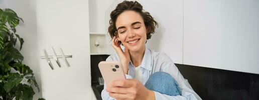 retrato do mulher sentado às casa com Móvel telefone, conectados compras em Smartphone aplicativo, gastos Tempo dentro de casa foto