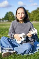 positivo hipster ásia garota, jogando ukulele e fazer rostos, cantando e sentindo-me feliz foto