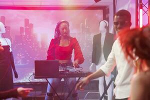 mulher dj usando misturador console para mistura faixas em etapa às Boate discoteca Festa. africano americano músico dentro fones de ouvido pressionando botões em eletrônico música estação às clube foto