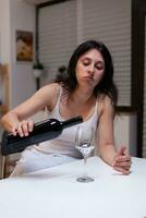 alcoólico mulher tendo garrafa do vinho e vidro sentindo-me triste às lar. solitário pessoa bebendo bebida com álcool ser depressivo. adulto com vício sentindo-me emocional e chateado foto