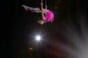 circo artista acrobata desempenho. a menina executa acrobático elementos dentro a ar. circo ginasta em a etapa foto