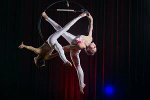 circo atriz acrobata desempenho. dois meninas executar acrobático elementos dentro a ar anel. foto