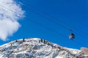 cabo carro para esquiadores contra a pano de fundo do uma azul céu e Nevado montanha encostas, Visão a partir de a inferior acima foto