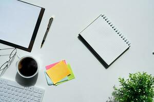 topo Visão acima do branco escritório escrivaninha mesa com teclado computador, caderno e café copo com equipamento de outros escritório suprimentos. o negócio conceito. ambiente de trabalho, plano deitar com em branco cópia de espaço foto