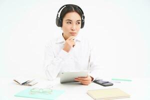 retrato do fofa escritório mulher dentro fones de ouvido, senta às ambiente de trabalho, trabalho com digital tábua, escuta para conectados curso, branco fundo foto