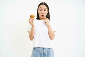 imagem do jovem moderno mulher com Bolinho, parece às delicioso pastelaria a partir de padaria com feliz face, branco fundo foto