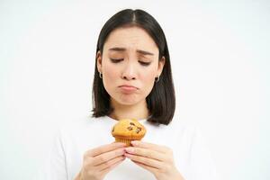 triste menina parece às saboroso Bolinho, também muitos calorias, ser em dieta, branco fundo foto