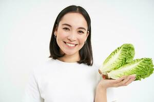 nutrição e saudável Comida. sorridente japonês mulher mostra repolho, fresco alface, isolado em branco fundo foto