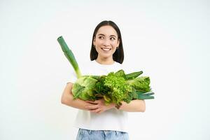 retrato do feliz jovem mulher em verde dieta, curtidas comendo orgânico comida, segurando fresco legumes a partir de jardim, alface, repolho, branco estúdio fundo foto