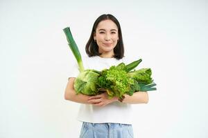 retrato do feliz jovem mulher em verde dieta, curtidas comendo orgânico comida, segurando fresco legumes a partir de jardim, alface, repolho, branco estúdio fundo foto