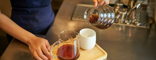 fechar acima do fêmea barista mãos derramando filtro café para dentro xícara, preparando ordem para cafeteria cliente foto