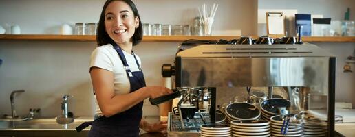 feliz sorridente barman, barista usando café máquina, preparar ordem, fazer cappuccino ou café com leite, vestindo azul avental foto